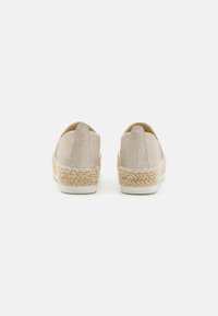 Zapatos tipo slip-on beige con un upper de tela texturizada, detalles de yute trenzado en la suela y una suela de goma blanca.
