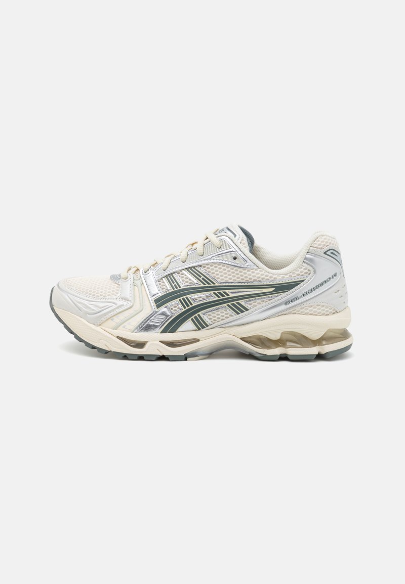O ténis de corrida apresenta um upper em malha off-white, detalhes em prata e riscas verde-escuras. Sola grossa com um padrão de borracha cinza texturizada para melhor aderência.