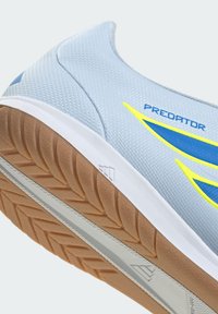 Chaussure de football en salle bleu clair avec semelle extérieure marron à crampons, semelle intermédiaire blanche et logo "Predator" jaune-bleu sur le côté.