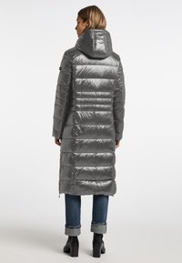 Długa, błyszcząca, szara kurtka puchowa z kapturem, z poziomym pikowaniem, bocznymi zamkami i prostym krojem, noszona na niebieskich dżinsach i czarnych butach.