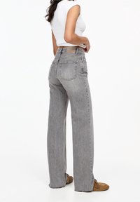 Jean gris taille haute coupe droite avec ourlet effiloché et poches arrière ; associé à un haut blanc ajusté sans manches et des chaussures marron.