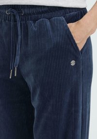 Námornícke kordové nohavice s ryhovanou textúrou, elastickým pásom, šnúrkou a bočnou vreckom. Obsahujú aj malý kovový logotyp.