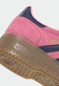 Παπούτσι Adidas με ροζ σουέντ επάνω μέρος, σκούρες μπλε δερμάτινες λεπτομέρειες και μοτίβο στη λαστιχένια σόλα. Διαθέτει χρυσό λογότυπο και υφή στο φινίρισμα.