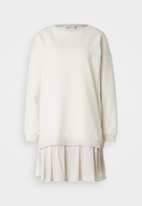 Felpa color crema con dettaglio gonna plissettata rosa chiaro, polsini a coste e zip laterali per un look stratificato. Texture liscia in tutto.