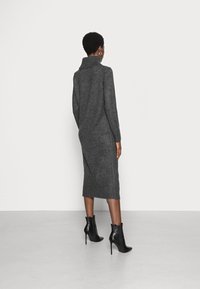 Abito di maglia grigio con un colletto alto, silhouette aderente e dettagli a coste all'orlo. Abbinato a stivali alla caviglia neri con tacco a spillo.