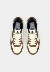 Λευκά και καφέ αθλητικά παπούτσια με διάτρητα πάνελ, επίπεδους κορδόνια και λογότυπο στο πλάι. Μαλακός πάτος και διακοσμητικές λεπτομέρειες σε αντίθετο χρώμα.