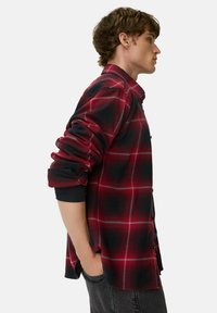 Rød og sort ternet flannel skjorte, knap-termineret design, oprullede ærmer, blød tekstur og subtile detaljer på manchetterne.