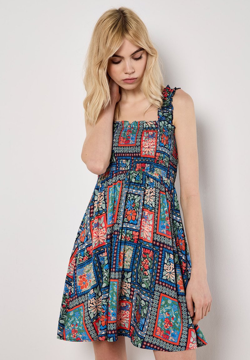 Vestido con estampado floral en colores azul, rojo y verde. Escote cuadrado, tirantes con volantes y falda acampanada. Hecho de tela ligera.