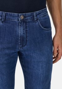 Jeans de mezclilla azul oscuro con un ajuste slim, que cuentan con cierre de botón, bolsillos laterales y un leve desgastado cerca de los muslos.
