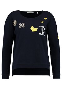 Marineblauwe trui met een getextureerd patroon, voorzien van verschillende geborduurde patches waaronder letters, sterren en vormen in geel en zilver.