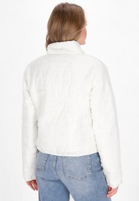 Giacca corta bianca imbottita con colletto alto, texture trapuntata e maniche lunghe. Abbinata a jeans in denim blu.