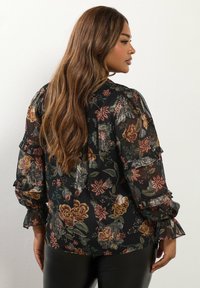 Blusa nera trasparente con motivi floreali in tonalità di rosso, verde e oro. Presenta maniche a sbuffo e una vestibilità ampia. Tessuto testurizzato.