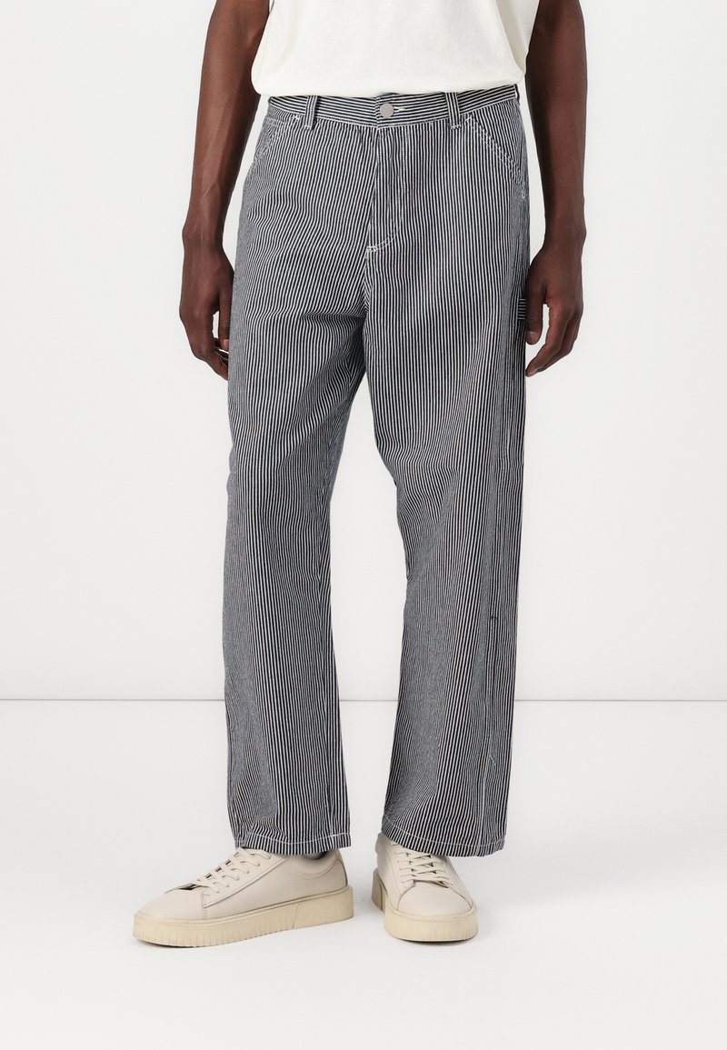 Striped trousers in blue and white cotton, featuring a relaxed fit, front pockets, and a button closure, styled with beige sneakers.