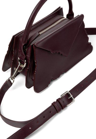 Sac à main en cuir bordeaux foncé avec poignée supérieure, bords de rabat irréguliers, fermeture éclair argentée et bandoulière réglable avec boucle.