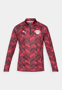 Rød og svart langermet jakke med glidelås og et fiskebensmønster, med Puma-logo og RB Leipzig-logo på brystet.