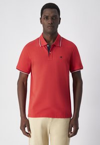 Rotes Polohemd mit einer Knopfleiste mit drei Knöpfen und einem marineblauen Kragen. Mit weißen und marineblauen Streifen an den Ärmeln. Weicher, leichter Stoff.