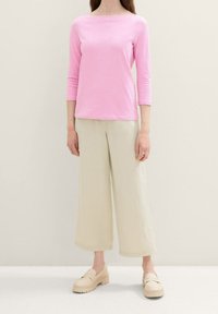 Long-sleeve pink top with a boat neckline, paired with wide-leg beige trousers and light-colored platform shoes. Smooth, casual fabric.