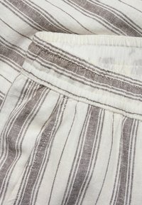 Gestreifter Stoff mit abwechselnd hellbeigen und braunen Linien, einem gerafften Bund und weicher Textur, der ein leichtes Design betont.