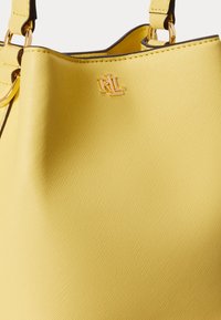 Gele leren handtas met gouden "RL"-logo en bijpassende gouden metalen accenten op de schouderbanden.