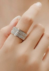 Anello d'argento con due fasce decorate con strass trasparenti e brillanti, indossato su un dito con unghie naturali e non trattate.