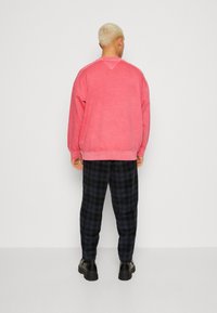 Sudadera de algodón rosa con cuello redondo, combinada con pantalones de cuadros negros que presentan tonos de azul y verde. Zapatillas negras completan el look.