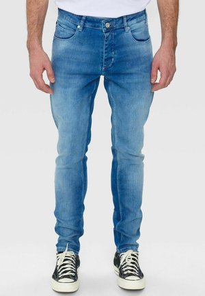Hellblaue, schlanke Jeans im Five-Pocket-Design mit subtilen Verblassungen und Wischdetails; kombiniert mit schwarz-weißen Sneakers.