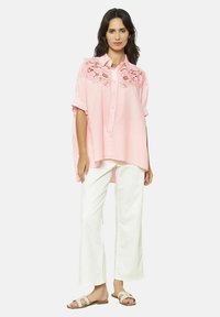 Camicia a quadri rosa con dettagli a fiori ritagliati sulle maniche, colletto abbottonato, vestibilità rilassata, abbinata a pantaloni bianchi a gamba larga e sandali.