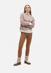 Suéter de forro polar marrón claro sobre una camisa blanca, combinado con leggings marrones y zapatillas de animal print con calcetines ribeteados color crema.