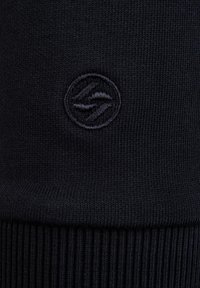 Gebreide muts in donker marineblauw, met een verhoogd, ton-sur-ton logo. Het patroon heeft fijne ribbels aan de onderkant voor extra textuur.