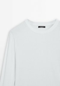 Pull blanc à manches longues avec col rond côtelé et une étiquette noire à l'intérieur de l'encolure.