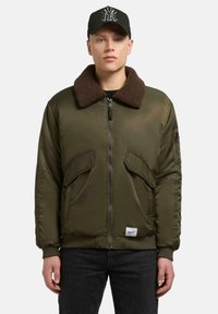 Olivgrüne Bomberjacke mit braunem Pelzkragen, Reißverschluss vorne, zwei großen Vorderentaschen und gerippten Bündchen, aus glattem Stoff gefertigt.