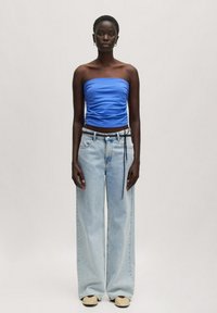 Blauwe strapless top met geplooide textuur, gecombineerd met wijde lichtkleurige denim jeans en tan instapschoenen, wat een moderne casual look presenteert.