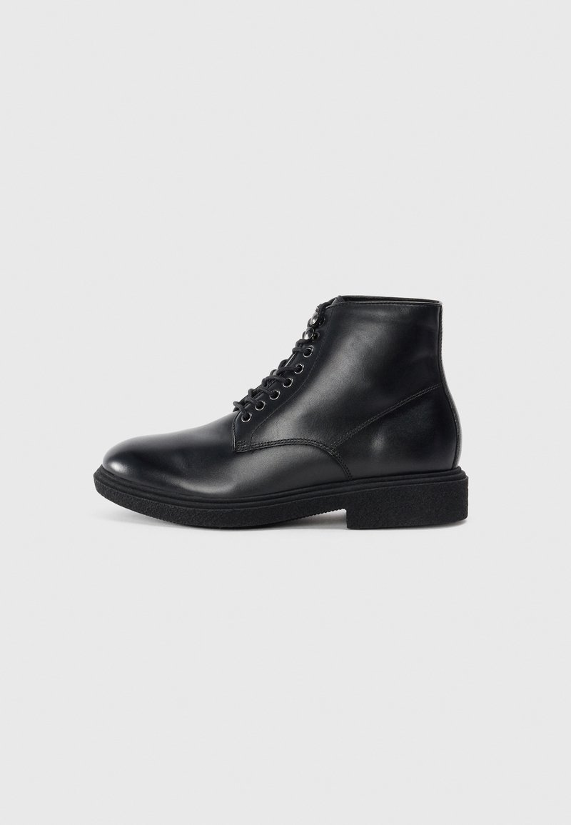 Bota de tobillo de cuero negro con cordones en la parte delantera, punta redondeada, suela texturada y hardware de ojal mínimo. Acabado liso con costuras sutiles.