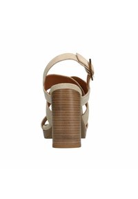 Beige suède sandaal met een bruine, gestructureerde hak en enkelbandje. Het ontwerp heeft gekruiste banden en een gespsluiting.