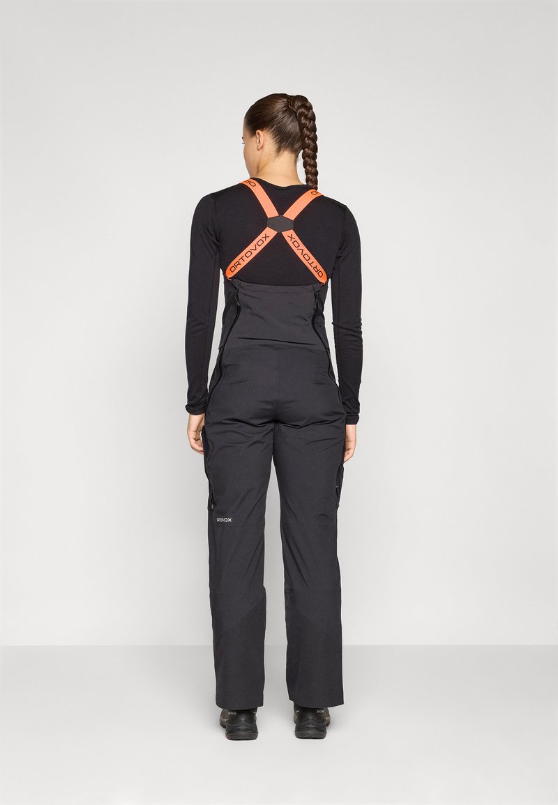 Schwarze Schneehosen mit verstellbaren orangen Trägern. Enthält Reißverschlüsse an den Seiten und reflektierende Akzente. Hergestellt aus langlebigem, wetterfestem Material.