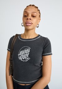 T-shirt preta cropped com impressão gráfica branca a dizer "SANTA CRUZ", apresentando costura em contraste e mangas curtas.