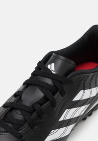 Zapatilla de fútbol negra con parte superior de cuero suave, cordones negros, rayas blancas y forro interior rojo. Texturizada para mayor agarre y soporte.
