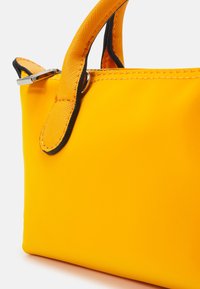 Sac à main jaune vif avec des poignées texturées bordées de noir et une quincaillerie argentée sur fond blanc.