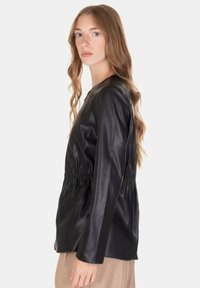 Giacca nera in pelle con vita aderente, maniche lunghe e texture liscia. Presenta una scollatura rotonda e un design minimalista.