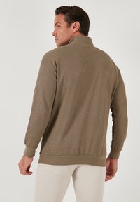 Pull-over à manches longues côtelé, olive, avec un col haut et des poignets élastiques, offrant une coupe décontractée et une texture douce.