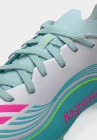 Ανοιχτό μπλε ποδοσφαιρικό παπούτσι με λείο συνθετικό επάνω μέρος, επίπεδα κορδόνια και ροζ λεπτομέρειες με κυματιστό μοτίβο. Διακριτά τα λογότυπα "F50" και "MESSI".