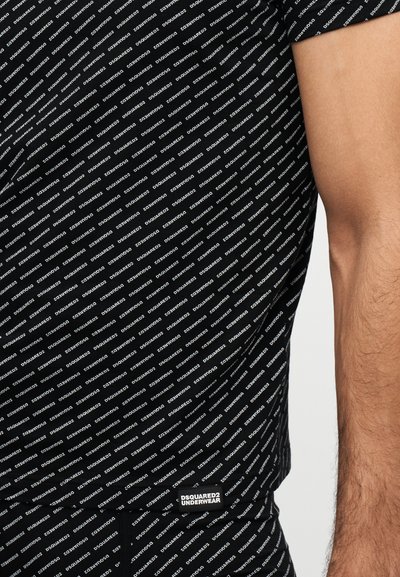 Tissu noir avec un motif de texte blanc répétitif "DSQUARED2" et une petite étiquette portant la mention "DSQUARED2 UNDERWEAR" près du bras nu d'une personne.