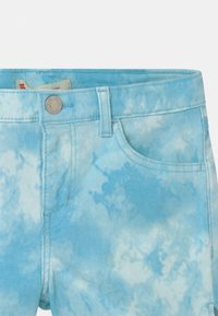 Shorts de denim de color azul claro con un patrón de tie-dye, que presentan un cierre de botón en la parte frontal, lazos para cinturón y bolsillos laterales. Textura suave.