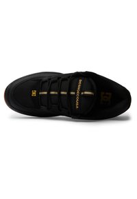 Black athletic shoe with a textured mesh upper, gold accents, lace-up design, and a rubber sole. Features a smooth toe cap and branded logo.