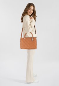 Sac en toile en cuir beige avec un design matelassé, des poignées doubles et une bandoulière amovible. Accentué d'un pendentif logo et de quincaillerie en métal.