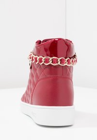Red high-top sneaker with quilted texture, glossy accents, and a gold chain detail around the ankle. White rubber sole.