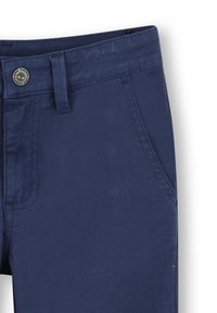 Marineblauwe katoenen broek met een zak aan de voorkant, een subtiele glans en een metalen logo knoop op de tailleband. Glad textuur en nauwsluitend ontwerp.