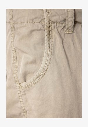 Beige stofshorts med en glat tekstur, der har en buet forlommer og detaljeret syning langs kanterne.