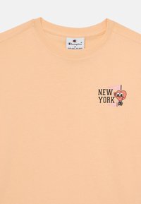T-shirt w kolorze brzoskwiniowym z bawełny z okrągłym dekoltem i grafiką na lewej piersi przedstawiającą napis "NOWY JORK" oraz postać serca w stylu kreskówkowym.