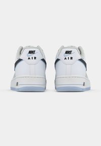 Nike Air Sneakers aus weißem Leder mit glatter Textur, ausgestattet mit einem schwarzen und blauen Akzent an der Ferse und einer klassischen flachen Gummisohle.